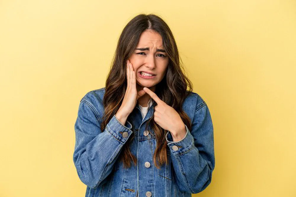 Woman experiencing tooth pain and pointing to her aching tooth