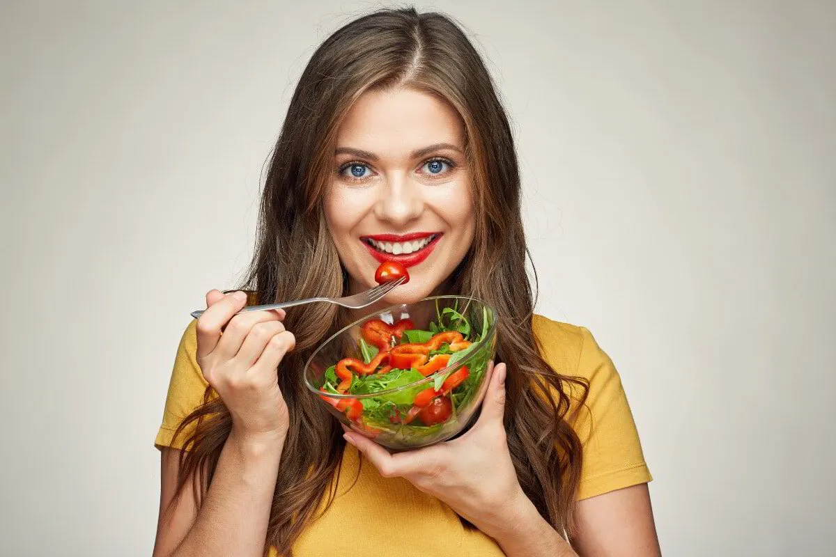 Smiling woman eating a fresh salad with tomatoes and leafy greens