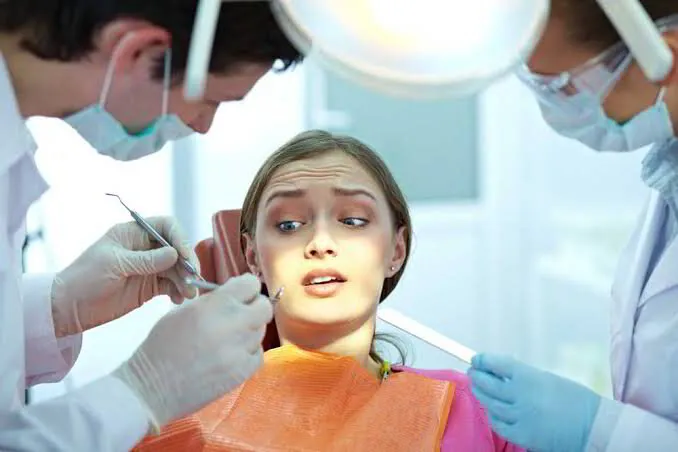 Nervous patient receiving dental treatment from two dentists in a dental clinic