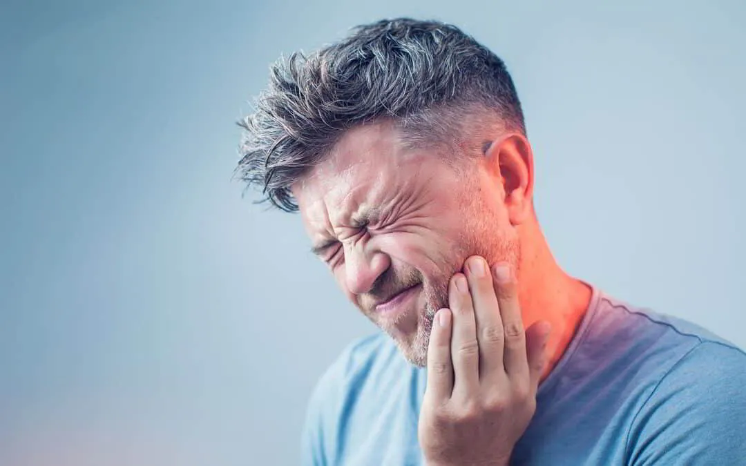 Man experiencing toothache and holding his cheek due to dental pain