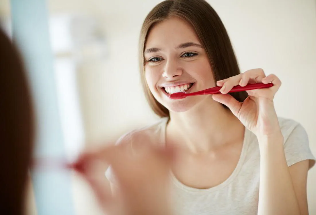 Young woman brushing her teeth in front of a bathroom mirror