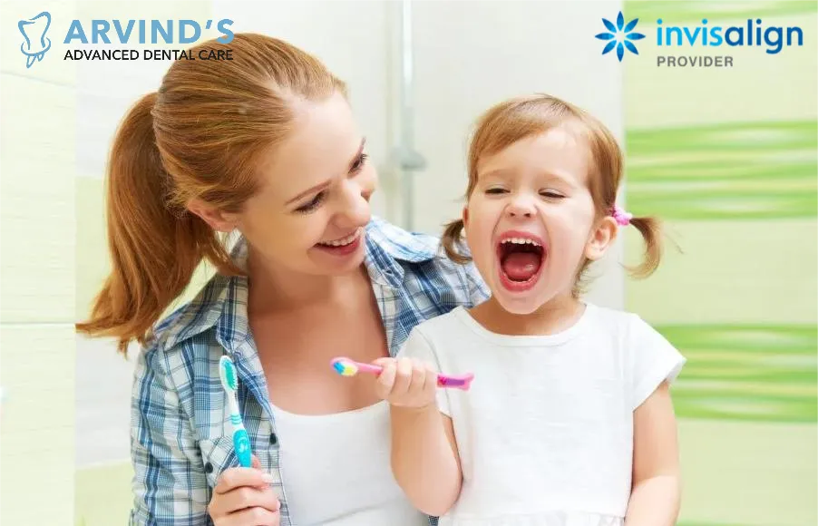 Mother helping her young daughter brush her teeth with a toothbrush