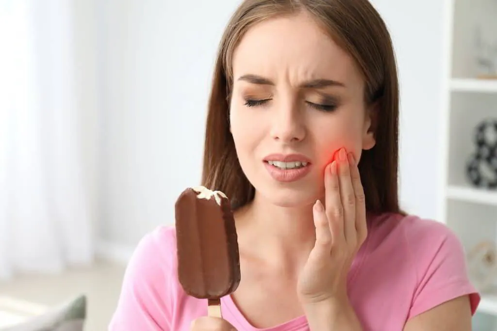 Woman experiencing tooth sensitivity and dental pain while eating ice cream