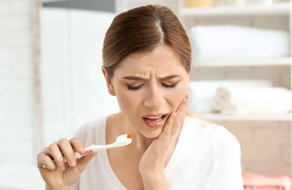 Woman experiencing severe tooth pain while brushing, indicating possible tooth nerve infection